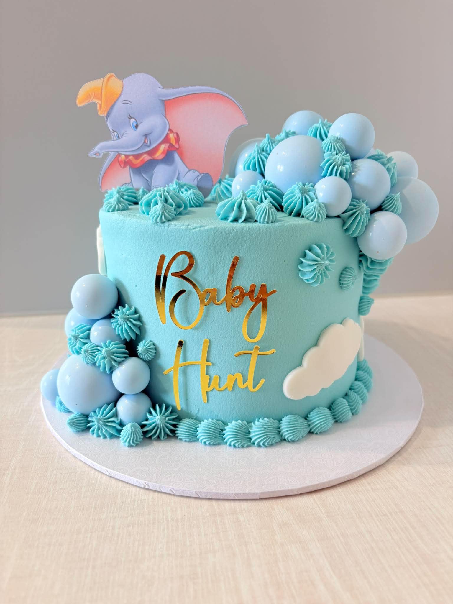 Blue Dumbo themed baby birthday cake with clouds and balloons