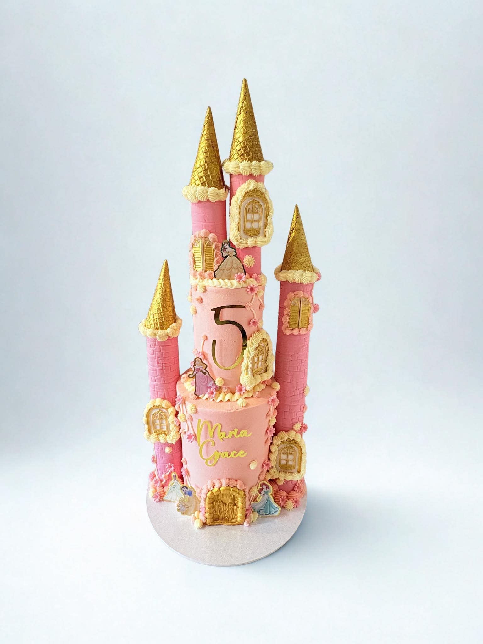 Pink princess castle cake with gold turrets and character decorations