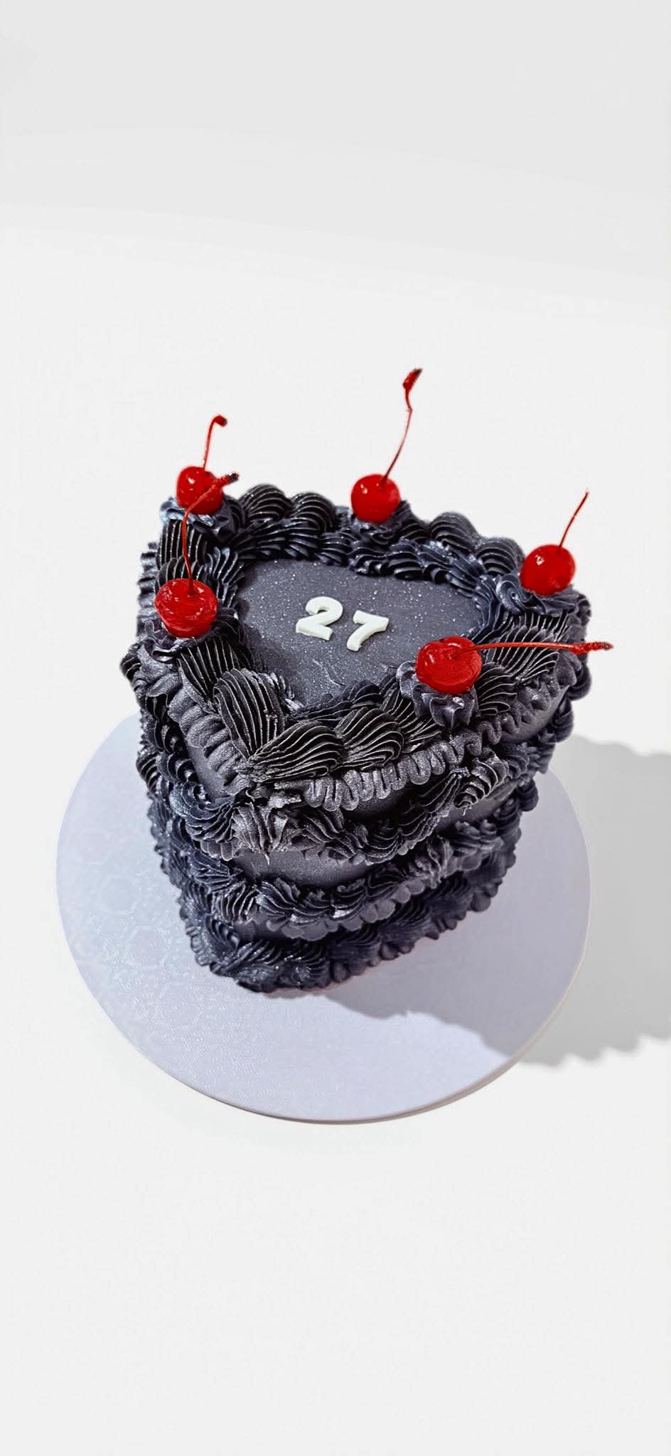Black heart-shaped piped cake topped with red cherries
