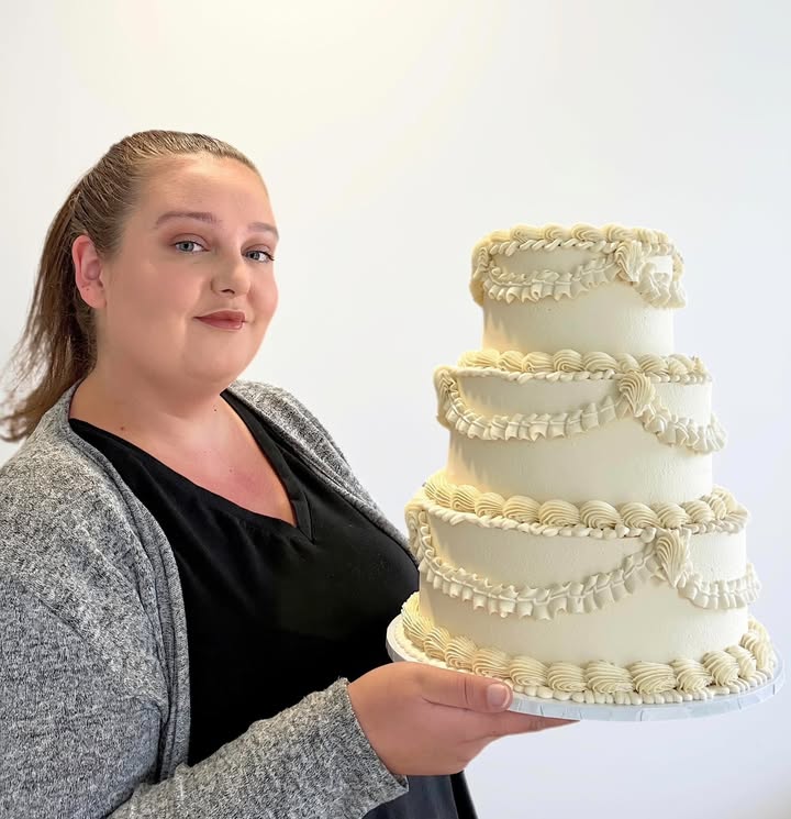 Chloe holding a three-tier ivory cake with delicate piped decoration