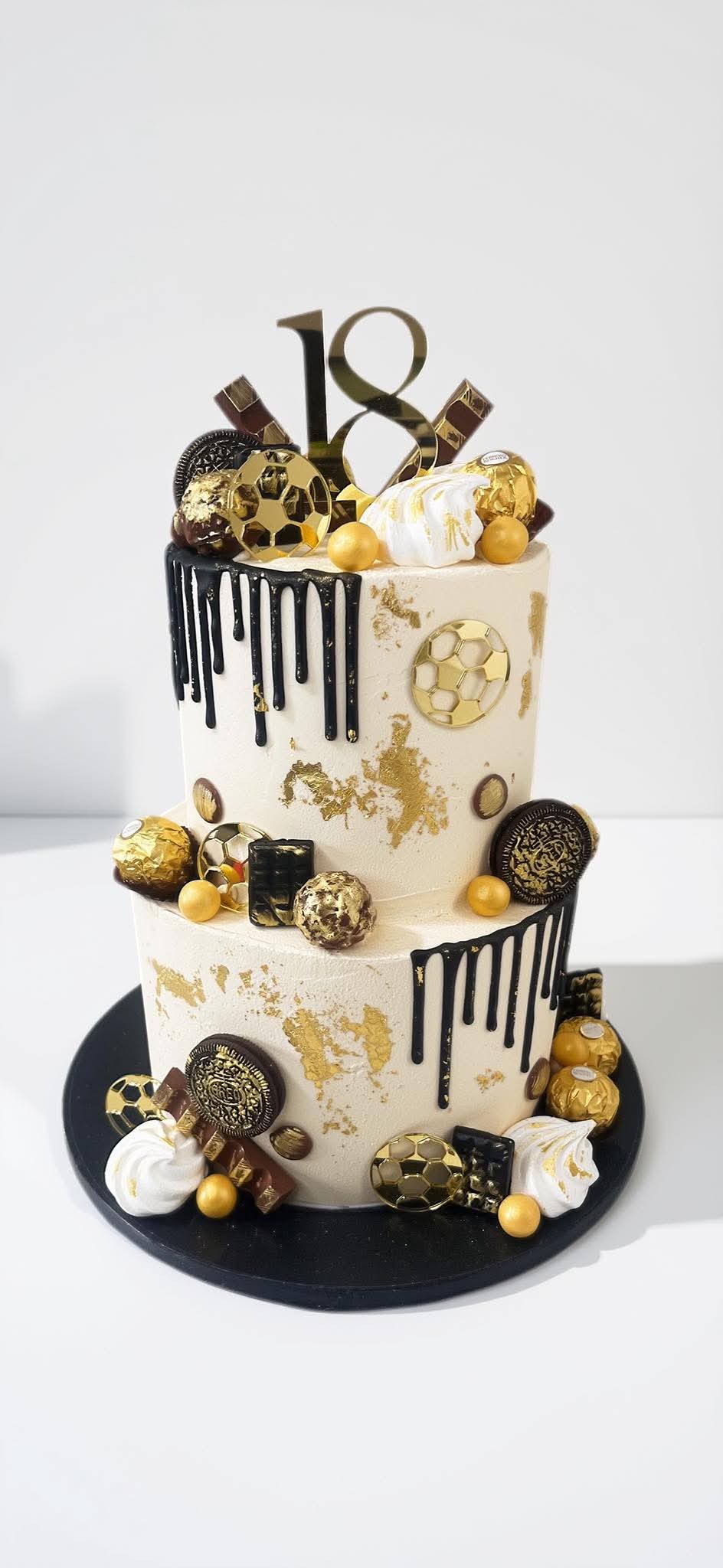 Two-tier ivory and black drip cake with gold football decorations